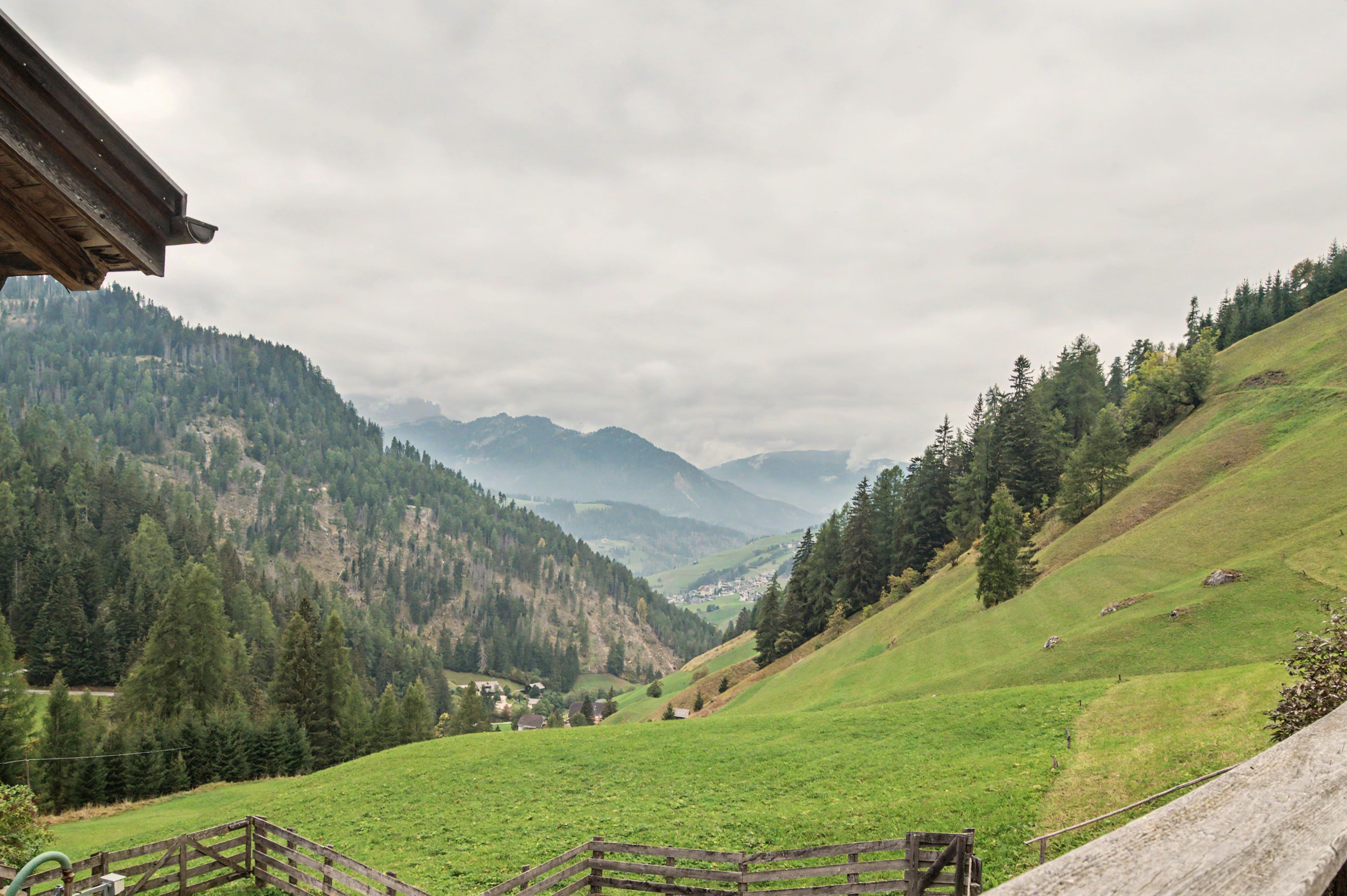 A rural landscape with a wooden fence, a grassy field, and a village in the valley.