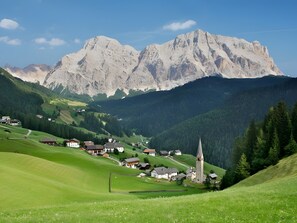 Un village rural avec des maisons et une église, entouré de montagnes et de verdure.