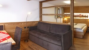 Una camera accogliente con soffitto in legno, un divano, un tavolo da pranzo con tovaglia rossa e una lampada da terra.