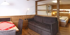 A cozy room with a wooden ceiling, a sofa, a dining table with a red table runner, and a floor lamp. - Apartment 'Wirthof  1' with Mountain View, Shared Terrace and Wi-Fi (La Valle)