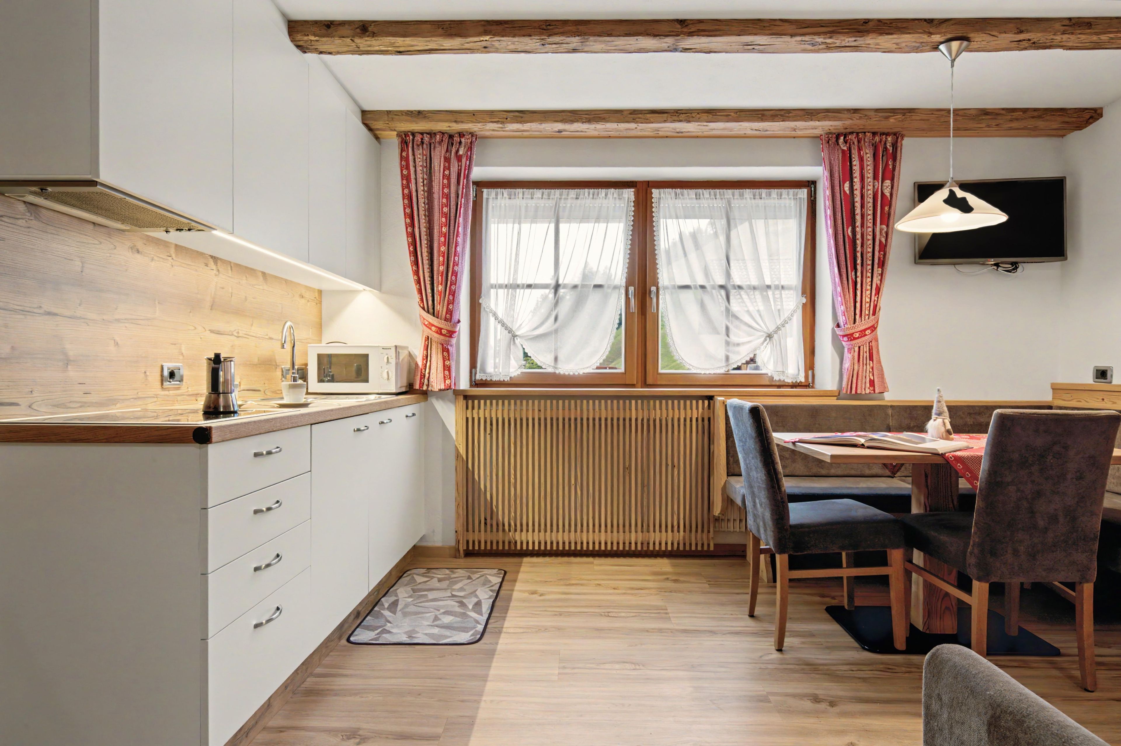 A kitchen with a wooden countertop, white cabinets, a built-in microwave, and a window with curtains.
