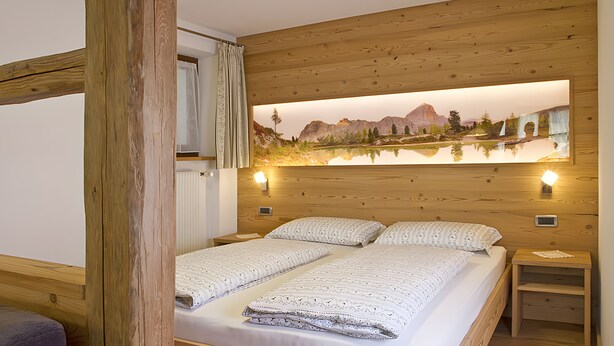 Un letto matrimoniale con copriletto bianco decorato, due comodini con lampade e un grande dipinto raffigurante un paesaggio sulla parete.