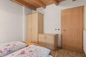 A bedroom with two beds, wooden wardrobe, and a door. - Apartment 'Wirthof  3' with Mountain View, Shared Terrace and Wi-Fi (La Valle)