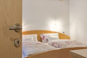 Eine Holztür mit Schlüsselloch und Griff, die zu einem Bett mit hölzernem Kopfteil und weißer Bettwäsche führt.