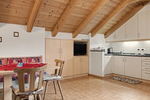 A kitchen with wooden cabinets, a dining table with chairs, and a television. - Apartment 'Wirthof  4' with Mountain View, Shared Terrace and Wi-Fi (La Valle)