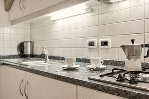 Une cuisine avec des murs recouverts de carreaux blancs, un plan de travail en granit, une machine à café et une bouilloire.