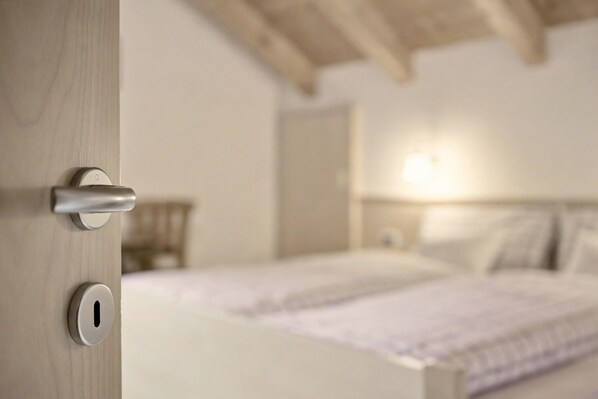 A bedroom with a wooden door, a bed with white bedding, and a nightstand with a lamp. - Apartment 'Wirthof  4' with Mountain View, Shared Terrace and Wi-Fi (La Valle)