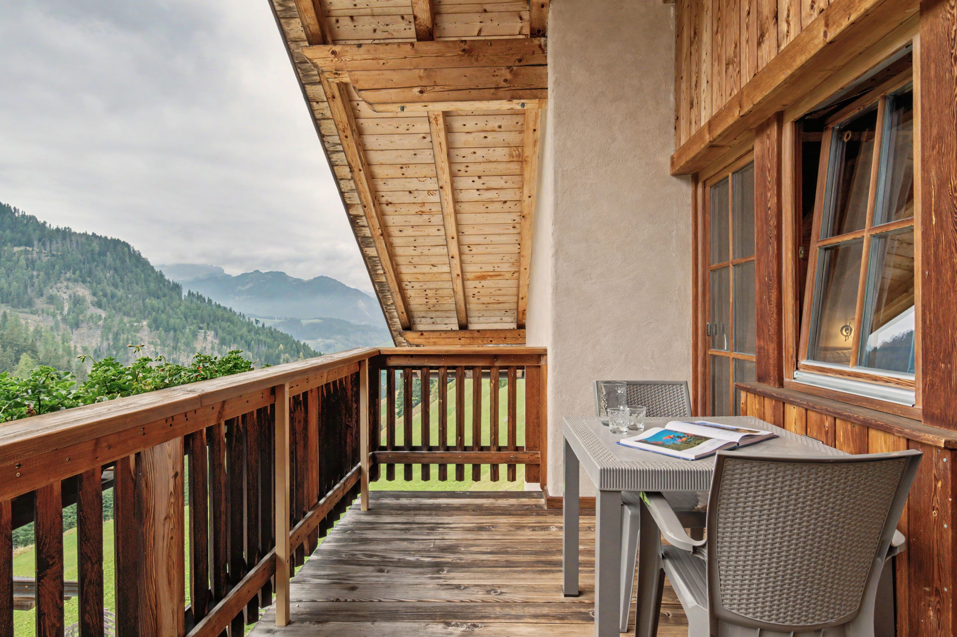 Un balcon en bois, agrémenté d’une table et de chaises, qui offre une vue sur un paysage montagneux.