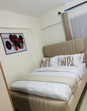 Ein Hotelzimmer mit Bett, Kopfstütze, einem Fenster mit Vorhängen und einem Wandbild.