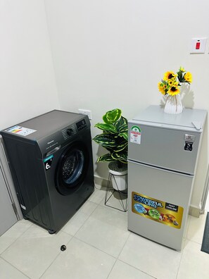 Habitación compacta con lavadora de carga frontal, un refrigerador pequeño y una planta en maceta.