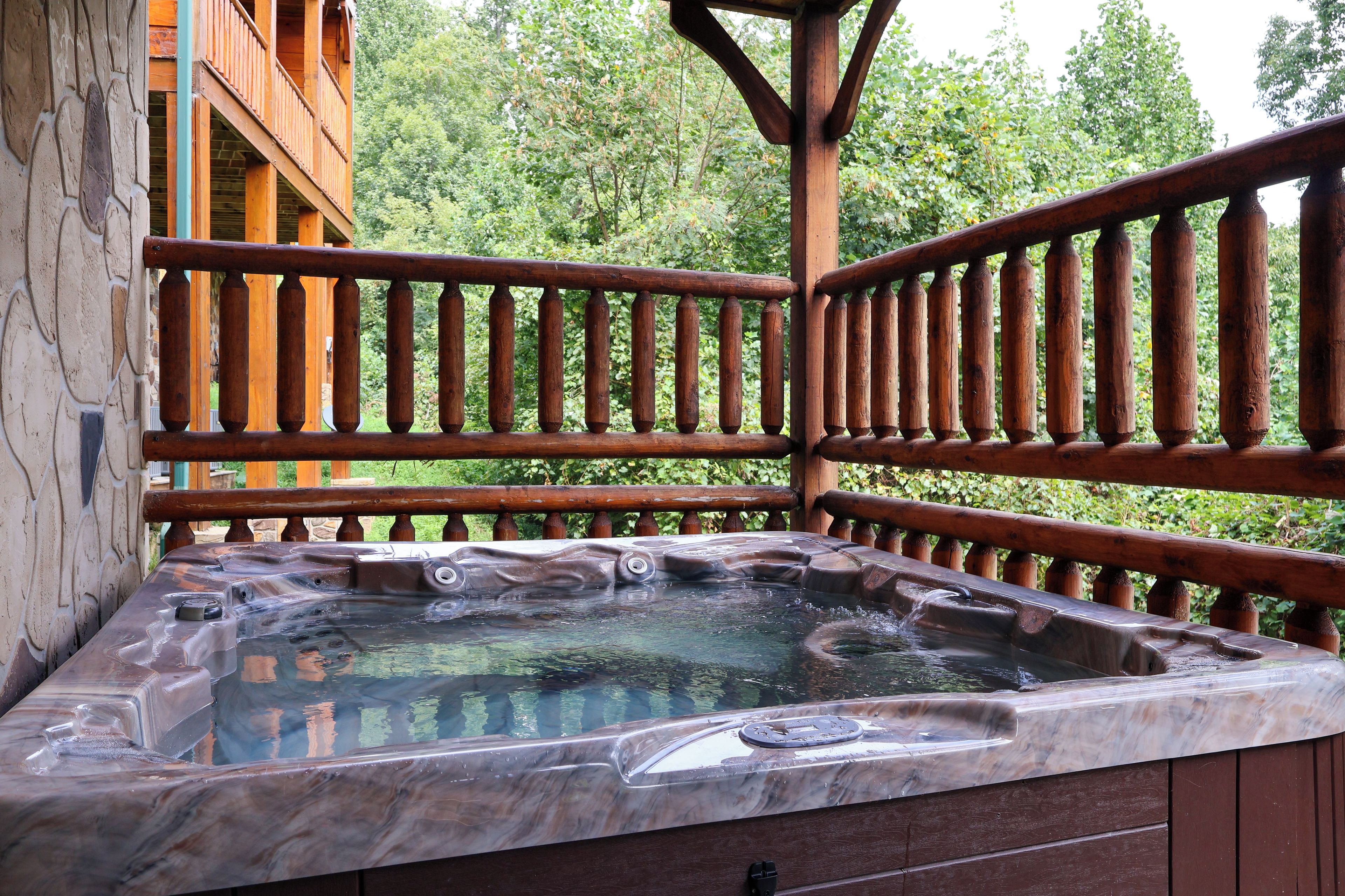 A hot tub on a wooden deck with a stone wall and a wooden railing.