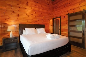A wooden-paneled bedroom with a bed, nightstand, and a door. - Private indoor pool, driving sim games, pool table, Smoky Mountain views! (Gatlinburg)