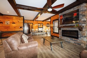 A cozy cabin interior with a leather sofa, wooden dining table, and a fireplace. - Private indoor pool, driving sim games, pool table, Smoky Mountain views! (Gatlinburg)