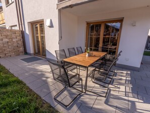 An outdoor patio with a wooden table and metal chairs, a brick wall, and a sliding glass door. - Anuk House Holiday Home With Mountain Views (Farchant)