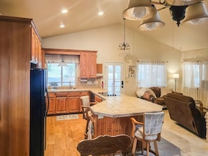 A spacious kitchen with wooden cabinets, a central island, and a dining area with chairs. - Lil Cottage - A Peaceful Country Retreat Near Yosemite and Sonora Pass (Jamestown)