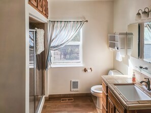 Ein Badezimmer mit Dusche, Toilette, Waschbecken und einem Fenster mit Vorhängen.
