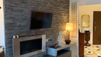 Un soggiorno moderno con parete in pietra, televisione a schermo piatto, camino e pavimento decorato.