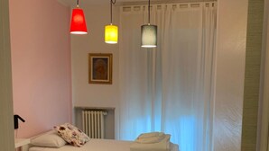 Quarto com duas camas, um radiador e uma janela com cortinas.