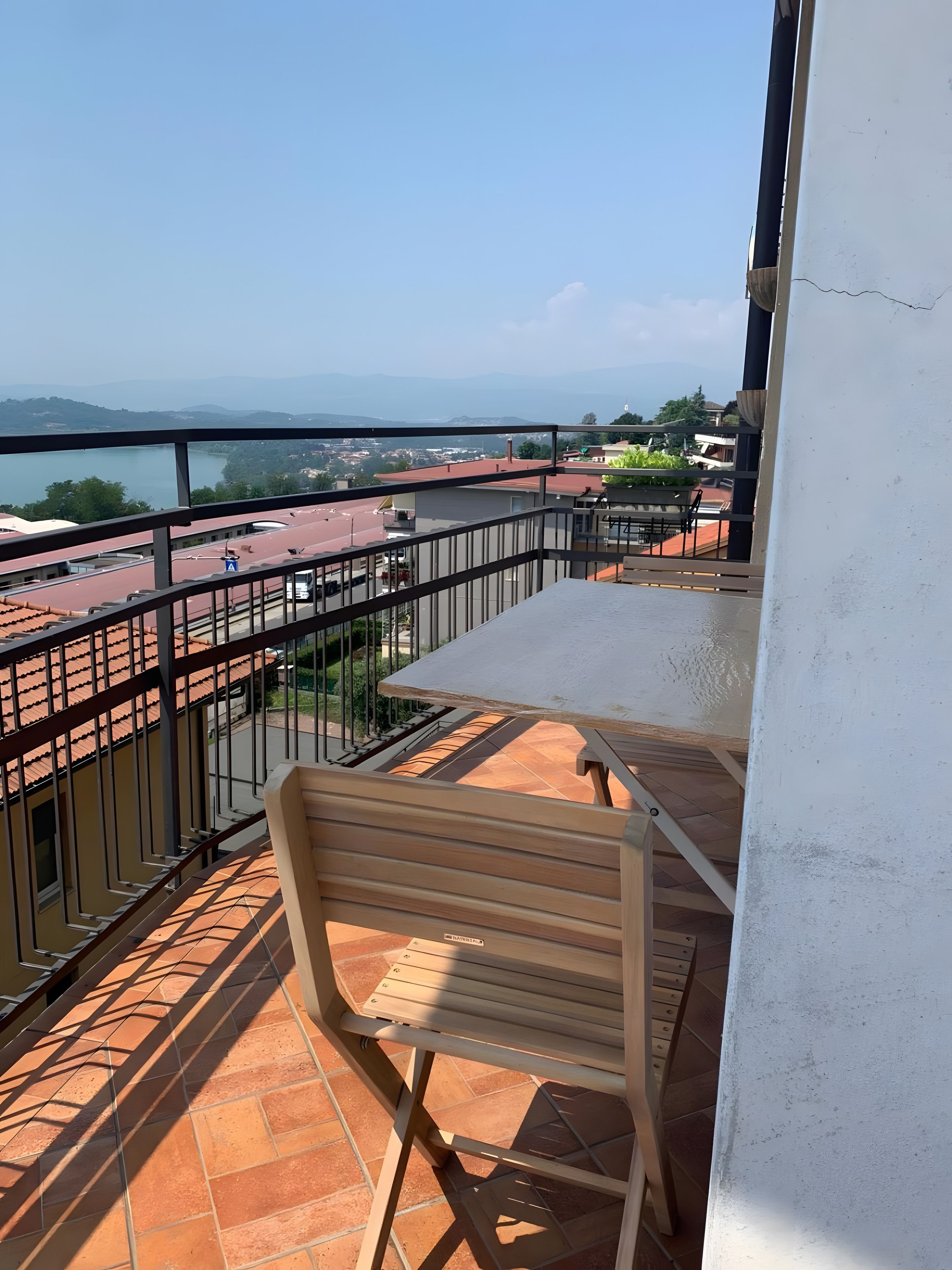 A balcony with a table and chair, overlooking a cityscape and a body of water.