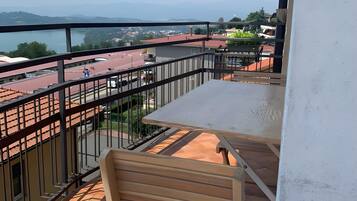 A balcony with a table and chair, overlooking a cityscape and a body of water.