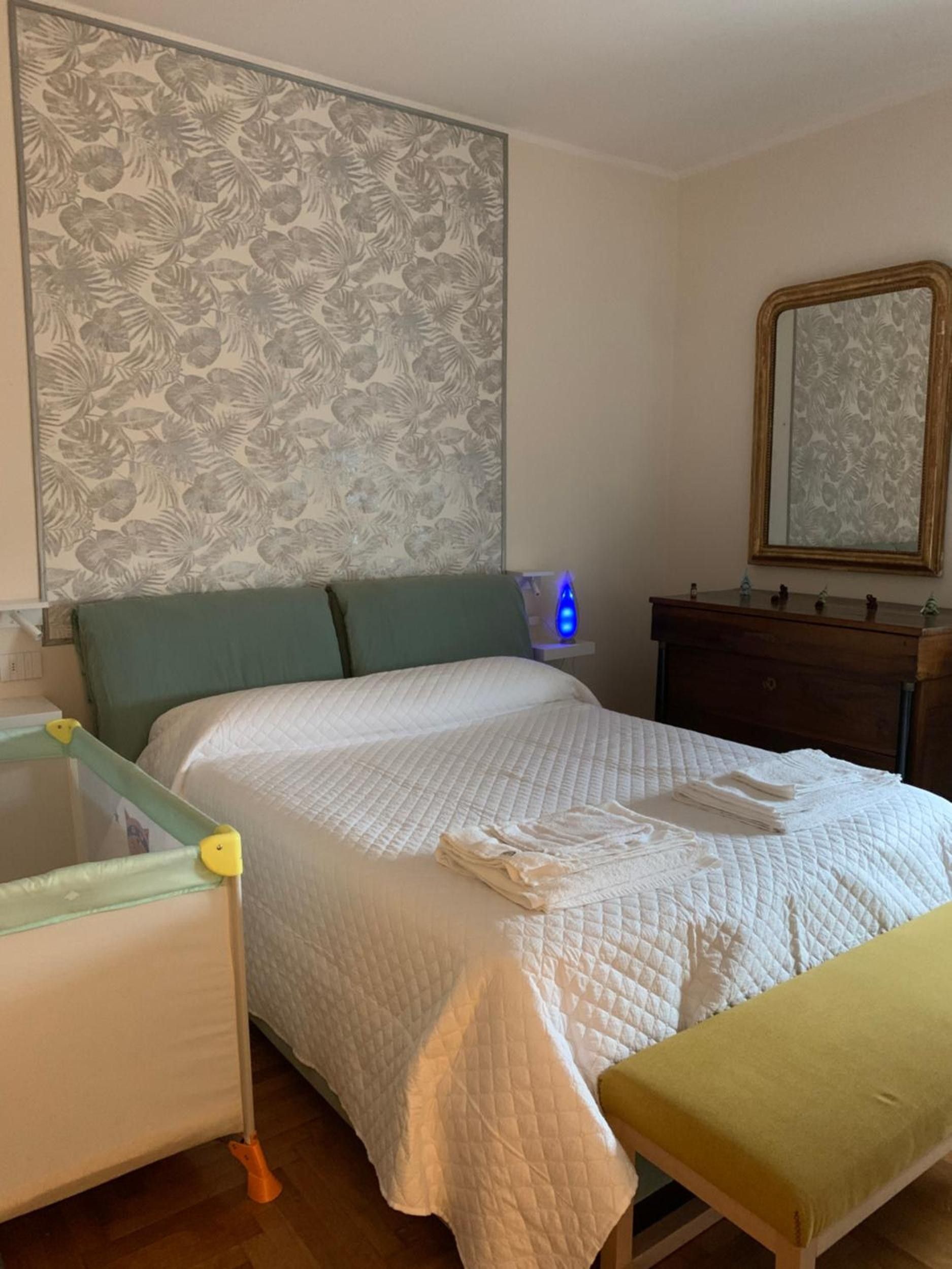 Una camera da letto con un letto, un comodino, uno specchio e una parete decorata con un motivo floreale.