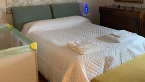 Een slaapkamer met een bed, nachtkastje, spiegel en een bloemenprint op de muur.