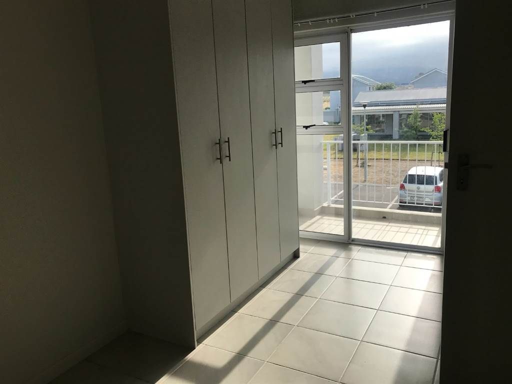 Ein Zimmer mit einer Schiebetür und einem Balkon, der einen Blick auf ein Auto und ein Gebäude bietet.