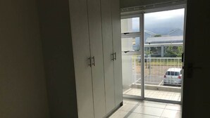 Una habitación con puerta de vidrio corrediza que da a un balcón con vista a un automóvil y un edificio.