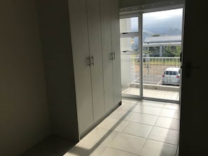 Una habitación con puerta de vidrio corrediza que da a un balcón con vista a un automóvil y un edificio.