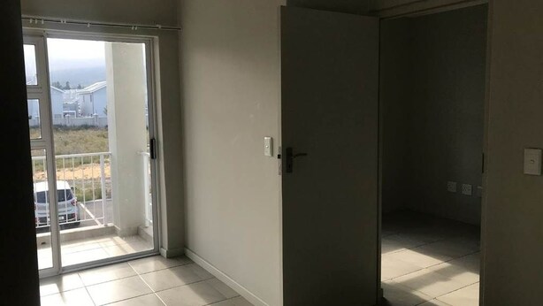 Una habitación con puerta corrediza de vidrio que da a un balcón, una puerta cerrada y piso de baldosas.