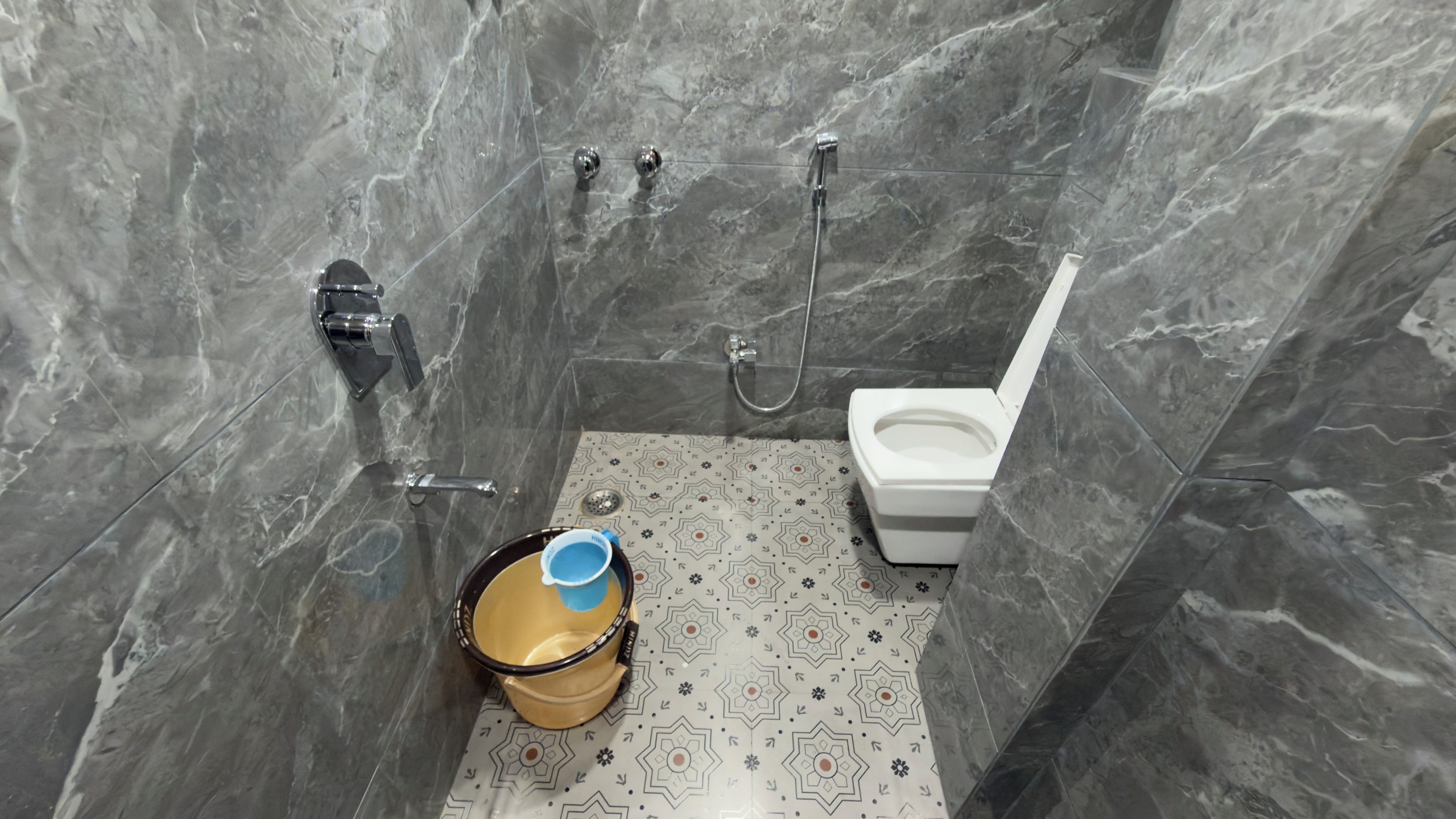 A bathroom with a toilet, shower, and a bucket on the floor.