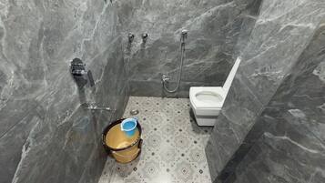 A bathroom with a toilet, shower, and a bucket on the floor.