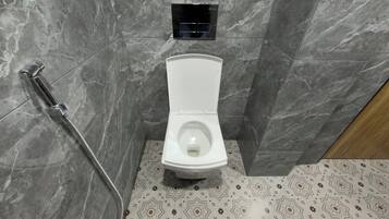Un baño con inodoro blanco, ducha con cabezal de ducha manual y piso estampado.