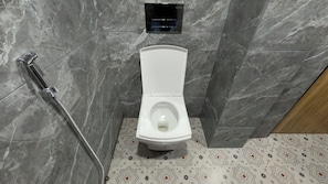 A bathroom with a white toilet, a shower with a handheld showerhead, and a patterned floor.