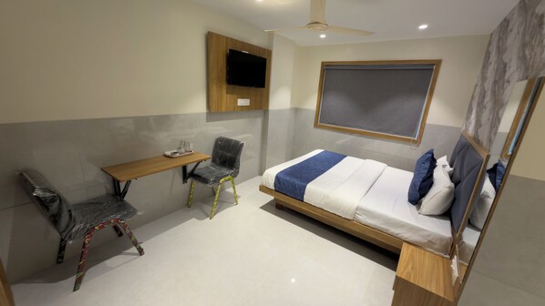 A compact hotel room with a bed, a desk, a chair, and a television.