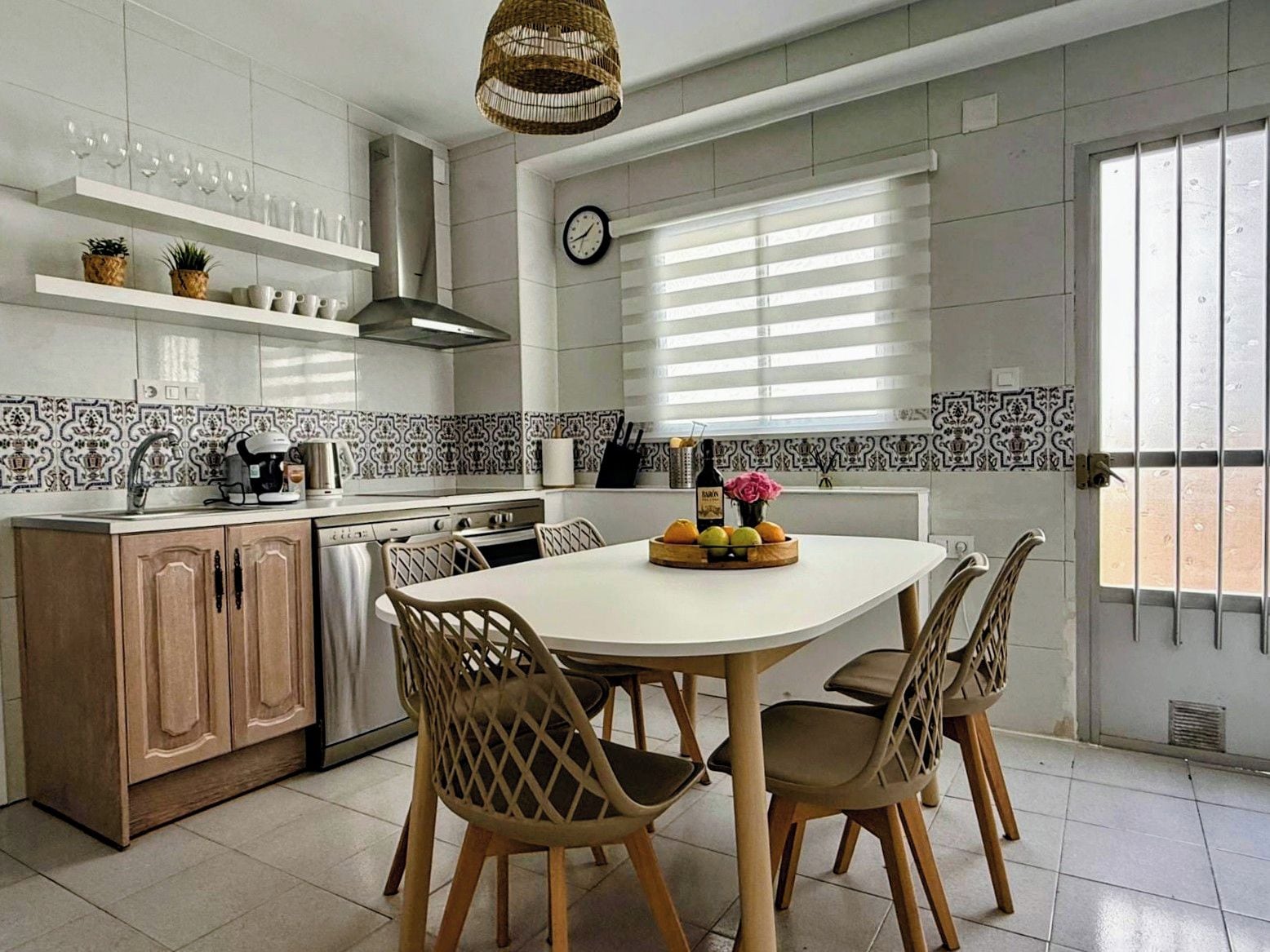 Een moderne keuken met een ronde eettafel, houten stoelen en diverse keukenapparaten.