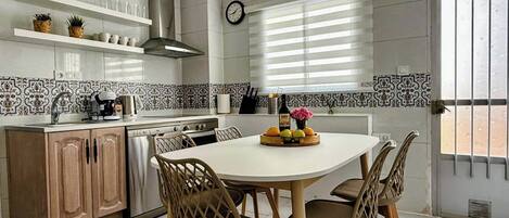 A modern kitchen with a round dining table, wooden chairs, and a variety of kitchen appliances.