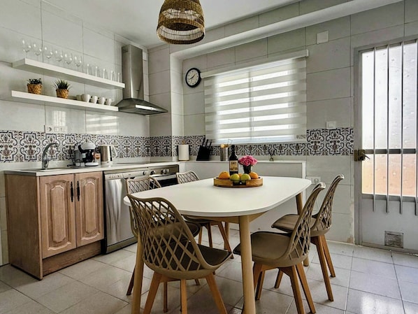 Een moderne keuken met een ronde eettafel, houten stoelen en diverse keukenapparaten.