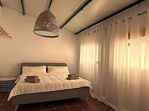 Een slaapkamer met een bed, witte gordijnen en een hanglamp.