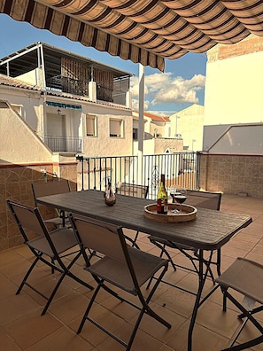 Een terras buiten met een tafel gedekt voor twee personen, een fles wijn en een glas.