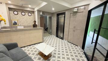 Zona de recepción de un hotel con mostrador, un sofá, suelo estampado y una puerta que da a un ascensor.