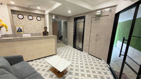 A hotel reception area with a reception desk, a sofa, patterned flooring, and a door leading to an elevator.