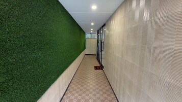 Un pasillo con pared verde artificial, suelo estampado y una puerta con panel de vidrio.