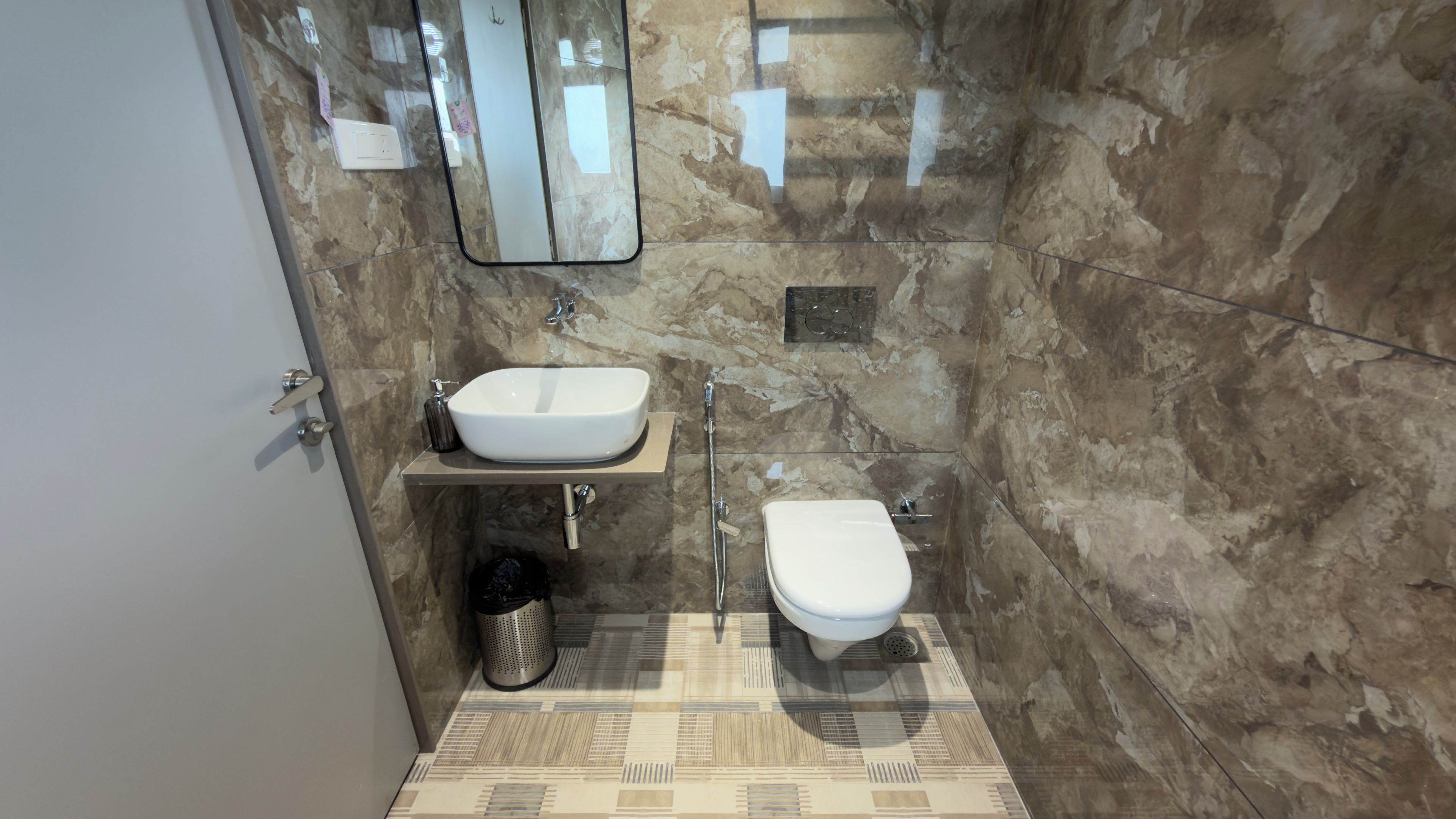 Un baño con pared de mármol, lavamanos blanco, inodoro y zona de ducha.