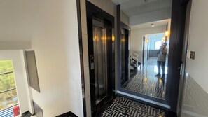 Ascensor moderno con pantalla digital, piso estampado y puerta de cristal que refleja a una persona.