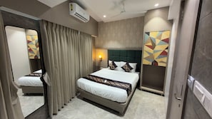 A hotel room with a bed, curtains, a wall-mounted air conditioner, a ceiling fan, and a geometric wall decoration.