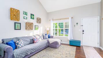 Una sala de estar con un sofá gris, cojines azules y rojos, un otoman azul, un tapete estampado y una puerta blanca.