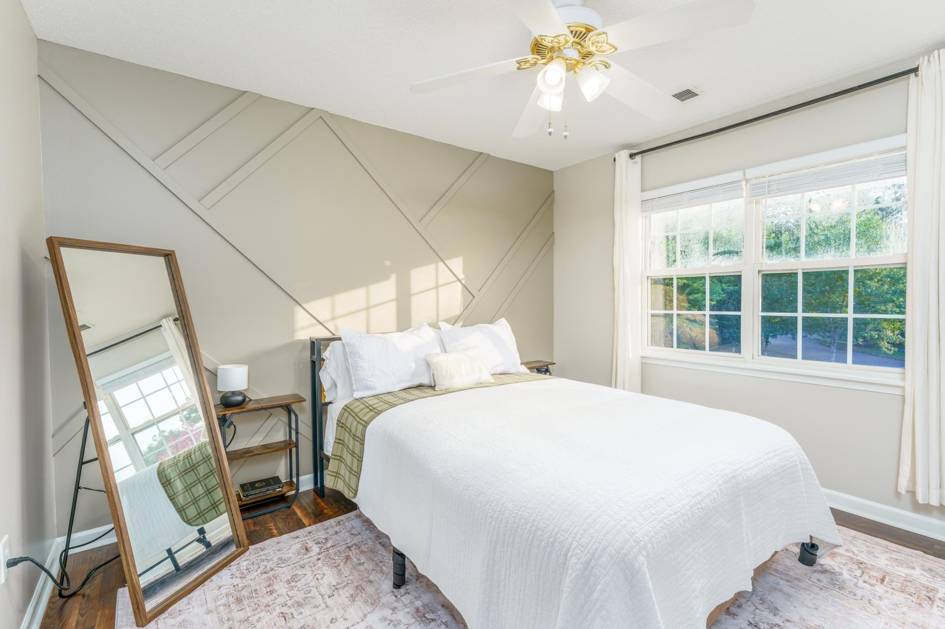 Une chambre à coucher comprenant un lit, un miroir, une table de chevet, une lampe et une fenêtre donnant sur un paysage verdoyant.