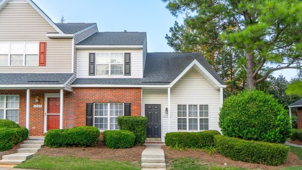 A two-story house with a brick facade, a front porch, and a well-maintained lawn. - Garden by the University (Charlotte)