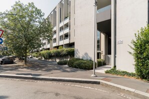 Un edifici modern amb diversos balcons, una zona d'aparcament i un cel serè.